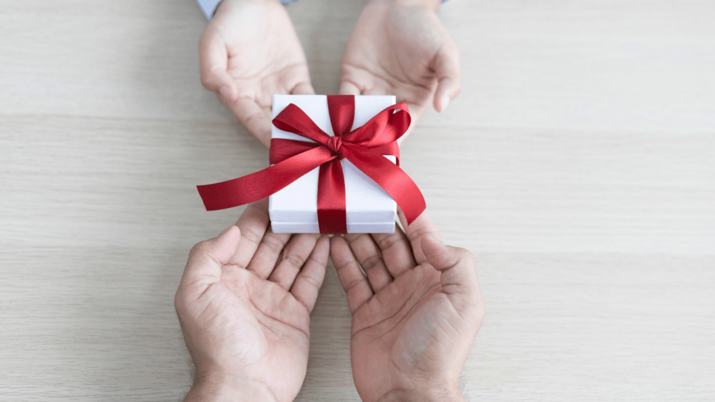 two hands holding a gift box with a red ribbon