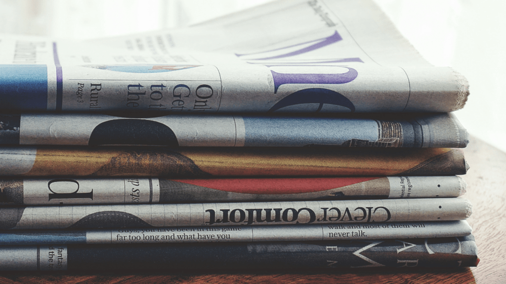 a stack of newspapers sitting on top of a wooden table