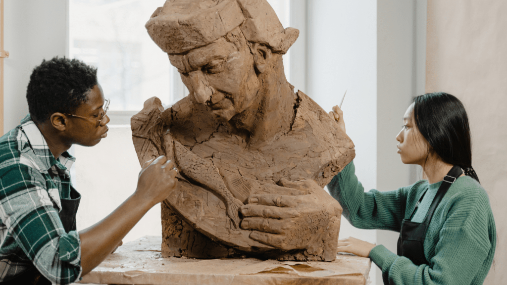 two people working on a clay sculpture of a man