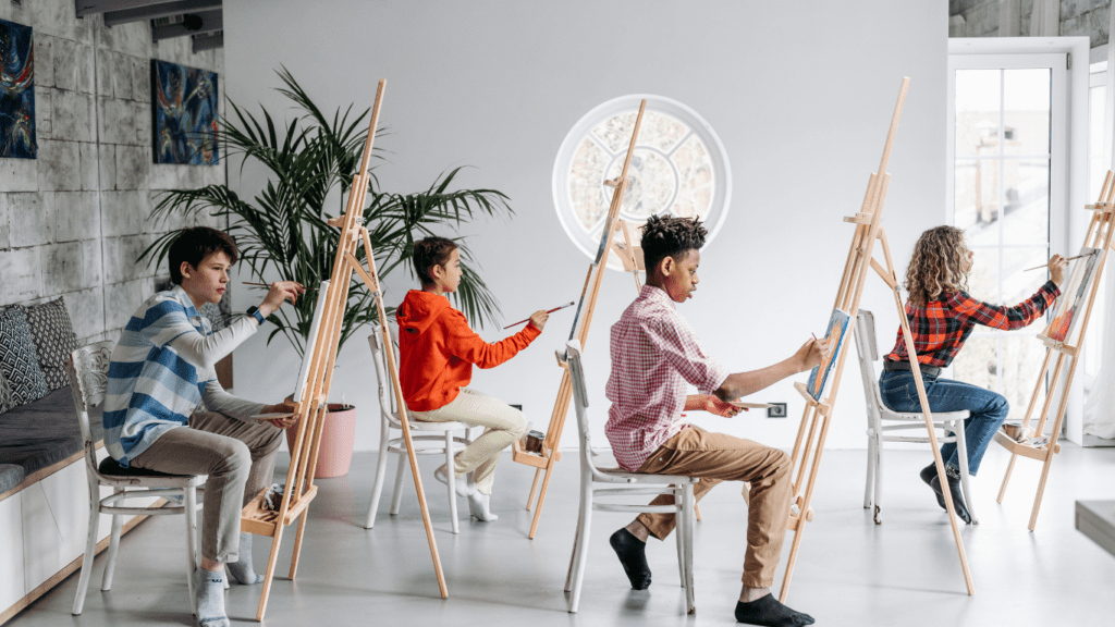 a group of people sitting on chairs and painting on easels