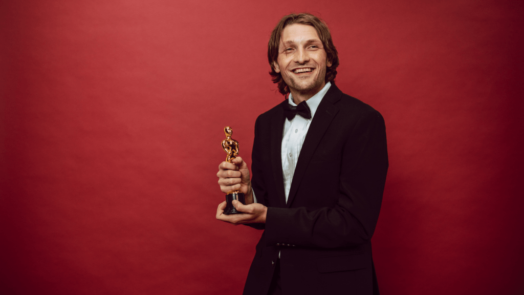 a person in a tuxedo holding a trophy in front of a red background