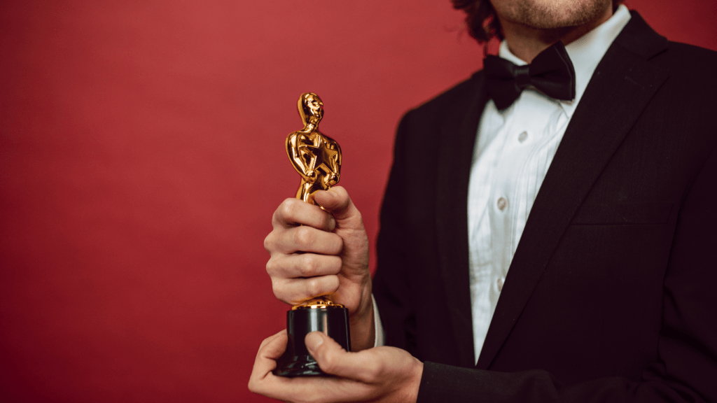 a person in a tuxedo holding a trophy in front of a red background