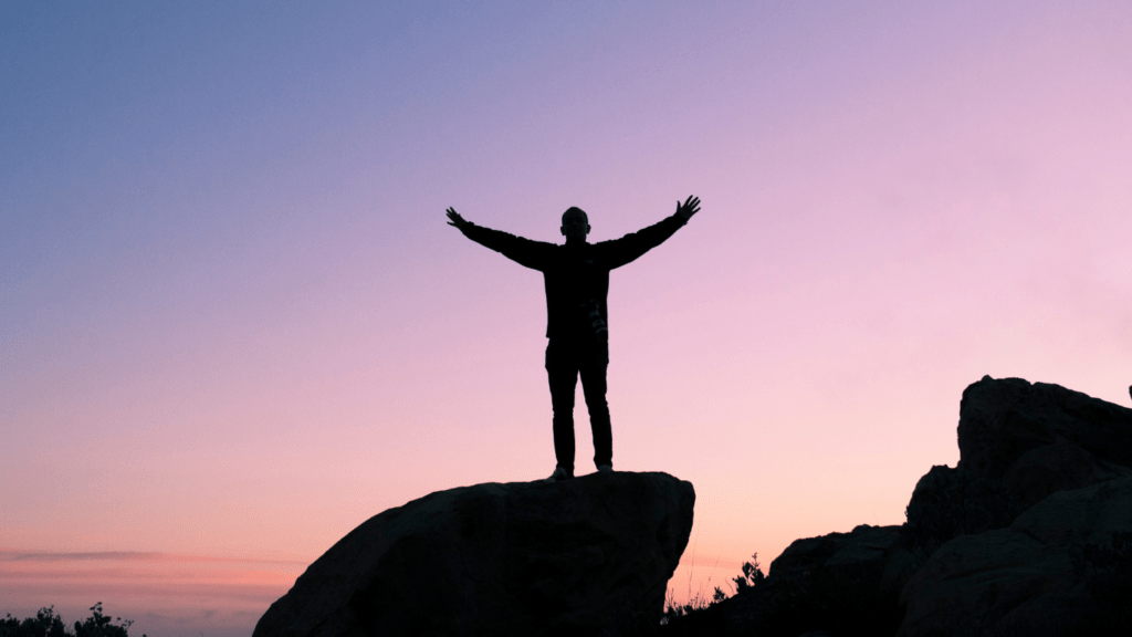 silhouette of a person standing on top of a mountain at sunset