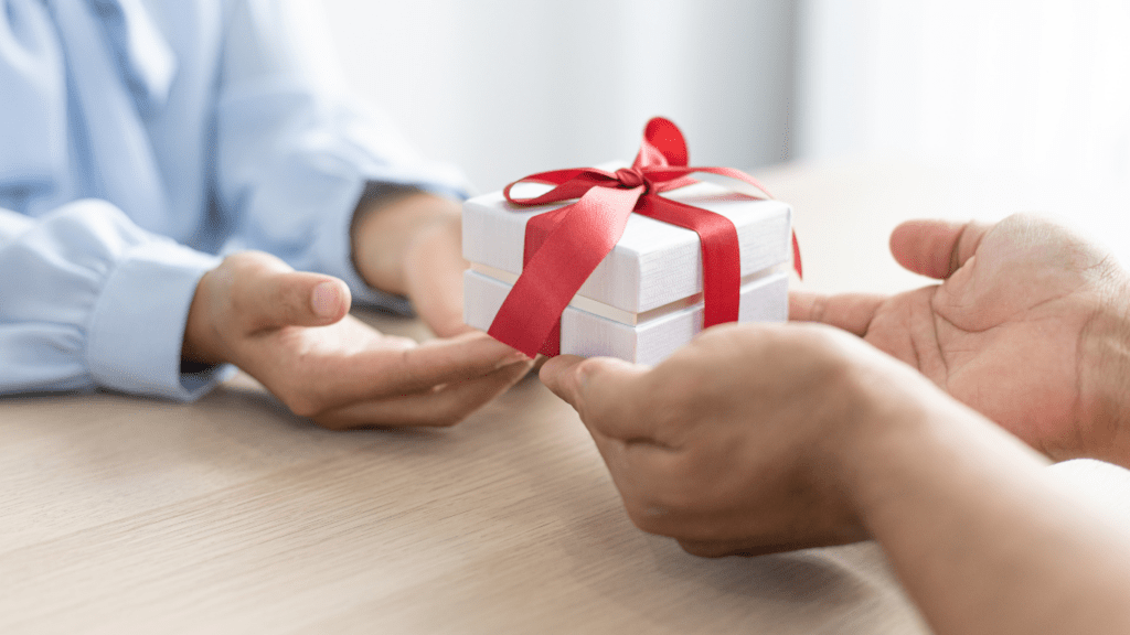 two hands holding a gift box with a red ribbon