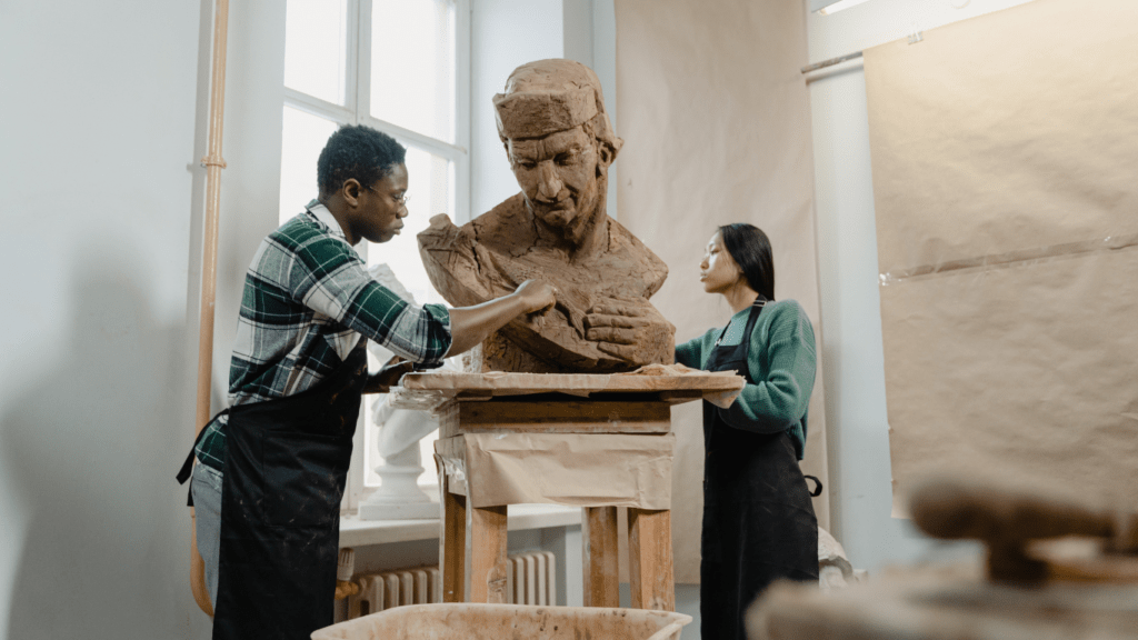 two people working on a clay sculpture of a man